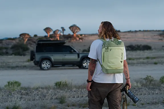 Abenteurer mit Gepäck und Kamera im Sonnenuntergang auf dem Weg zu einem Geländewagen